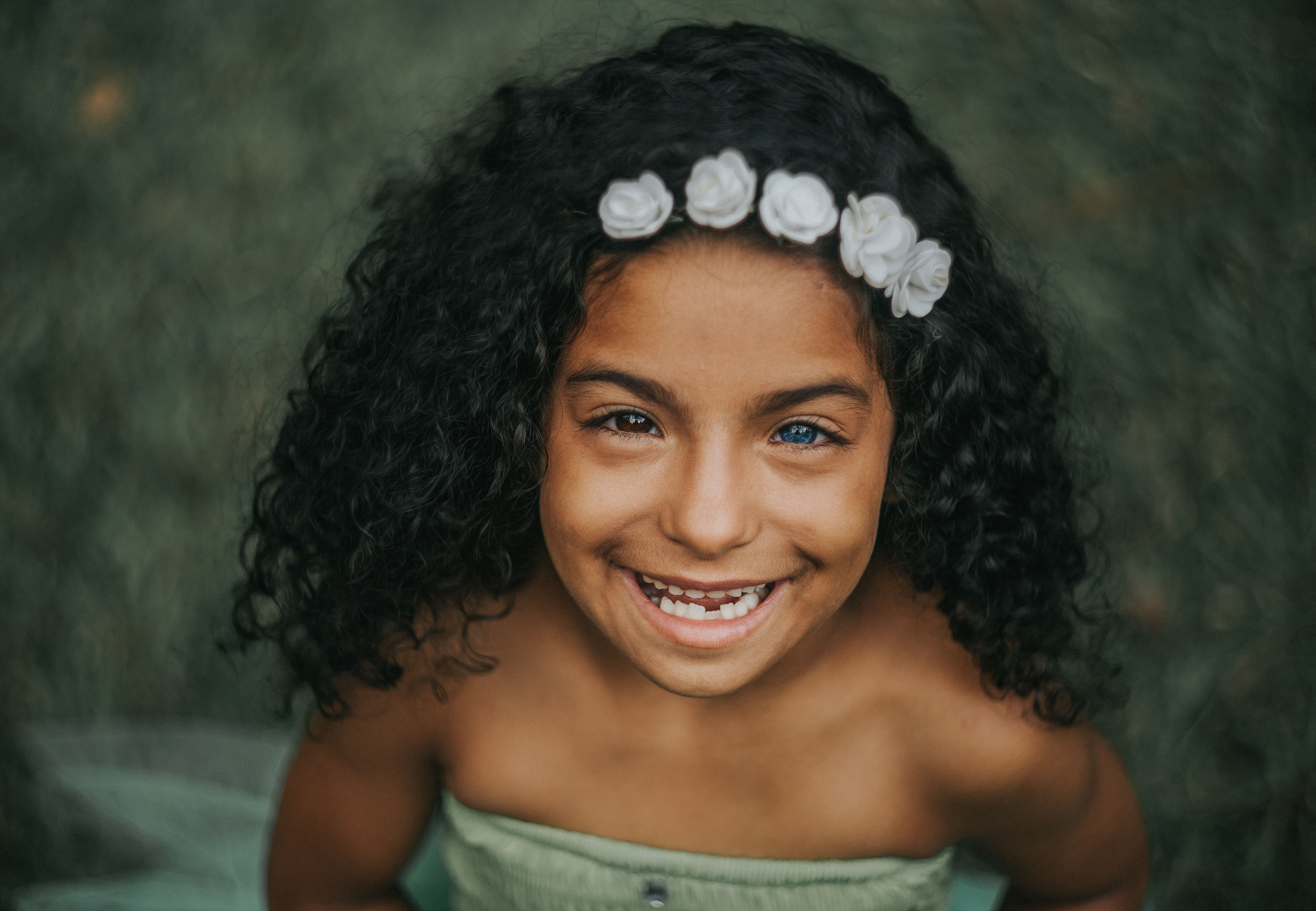 Happy child with curly hair and floral headband smiling outdoors.