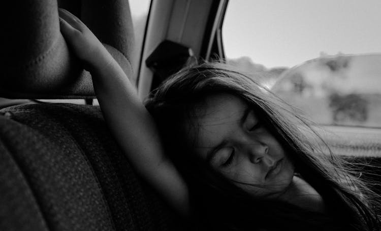 Grayscale Photo Of A Girl Sleeping Inside A Car