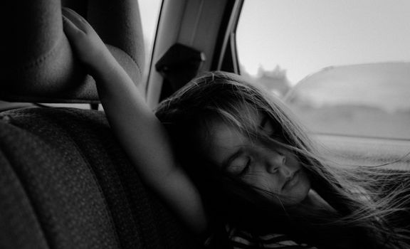 A young girl peacefully asleep in a car seat, captured in black and white.