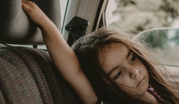 A young girl sits pensively in a car seat, gazing out the window.