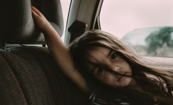 A young girl sits quietly in a car, gazing pensively out the window.