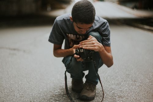 Free A young man crouching on the street intently checks his camera in an outdoor setting. Stock Photo