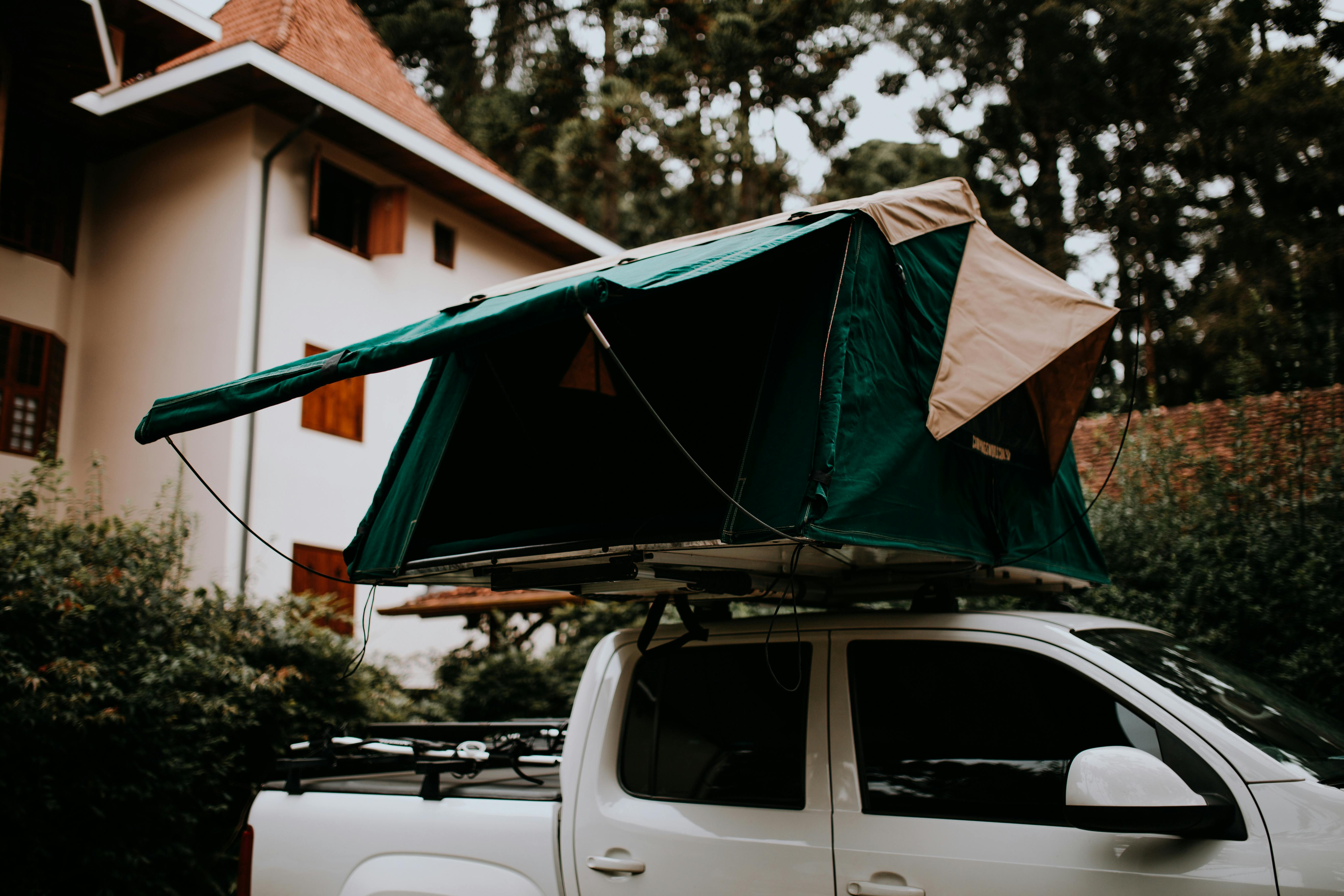 Free A rooftop camping tent set up on a white pickup truck parked outdoors near a house while performing some backyard survival prepping. 