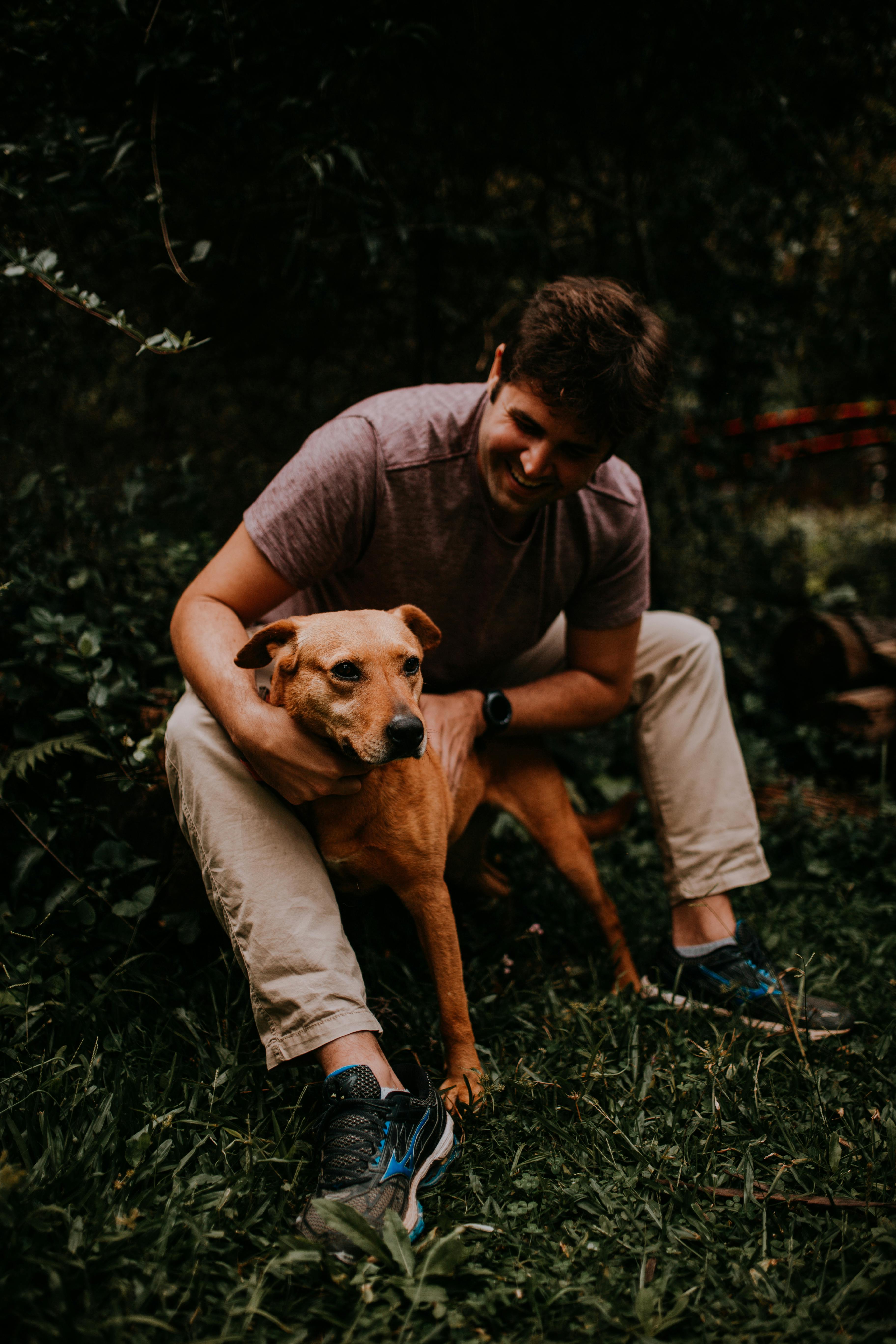 A man joyfully interacts with his pet dog in nature, surrounded by greenery.