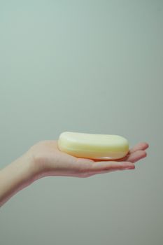 A hand holding a bar of white soap against a soft green background, emphasizing hygiene. - Fotografer Sidoarjo