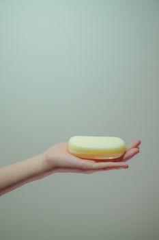 A hand holding a bar of soap against a minimalist, soft-toned background, emphasizing hygiene.