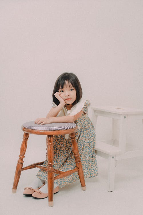 A Girl Sitting on White Step Ladder Leaning on a Wooden Chair