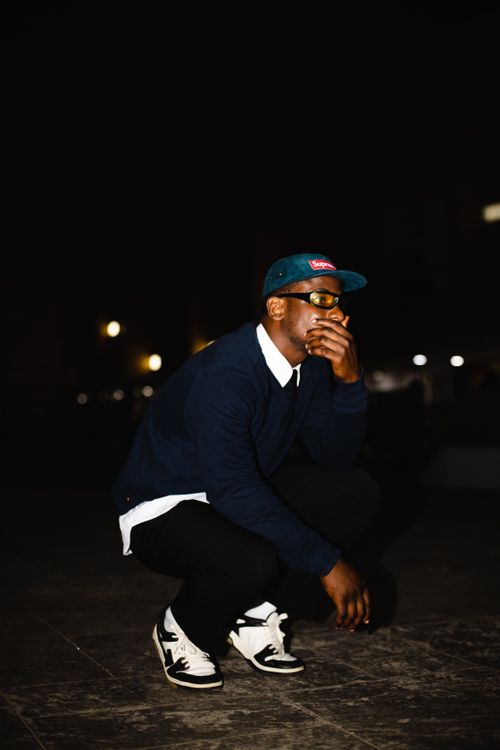 Free Stylish man in casual attire crouching on a city street at night, showcasing urban fashion. Stock Photo