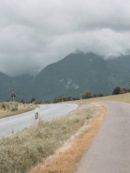 A winding road through lush green mountains under dramatic overcast skies, perfect for travel inspiration.