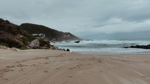 Free A scenic overcast beach in Kareedouw, South Africa, featuring waves, hills, and coastal houses. Stock Photo