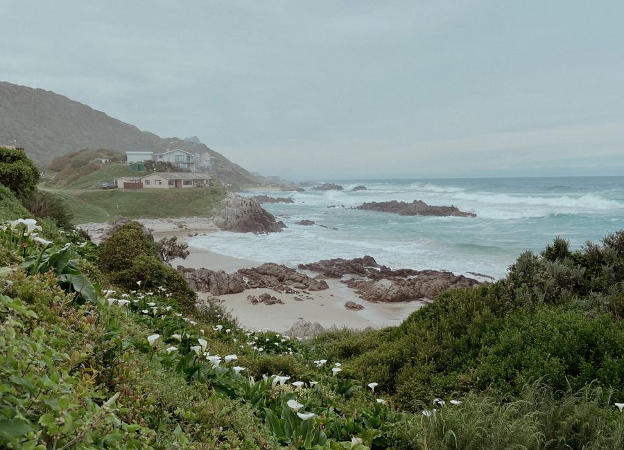 A tranquil coastal scene in Kareedouw, South Africa with waves, rocks, and greenery.