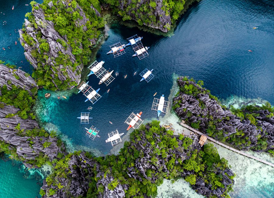 Stunning aerial shot of boats in a turquoise lagoon surrounded by rock formations in El Nido, Palawan, Philippines.