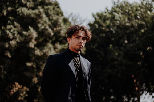 Free Portrait of a stylish man in a dark suit standing outdoors in natural sunlight. Stock Photo