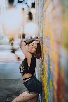 Stylish woman with short hair poses against a vibrant graffiti wall wearing denim shorts and fishnet stockings.