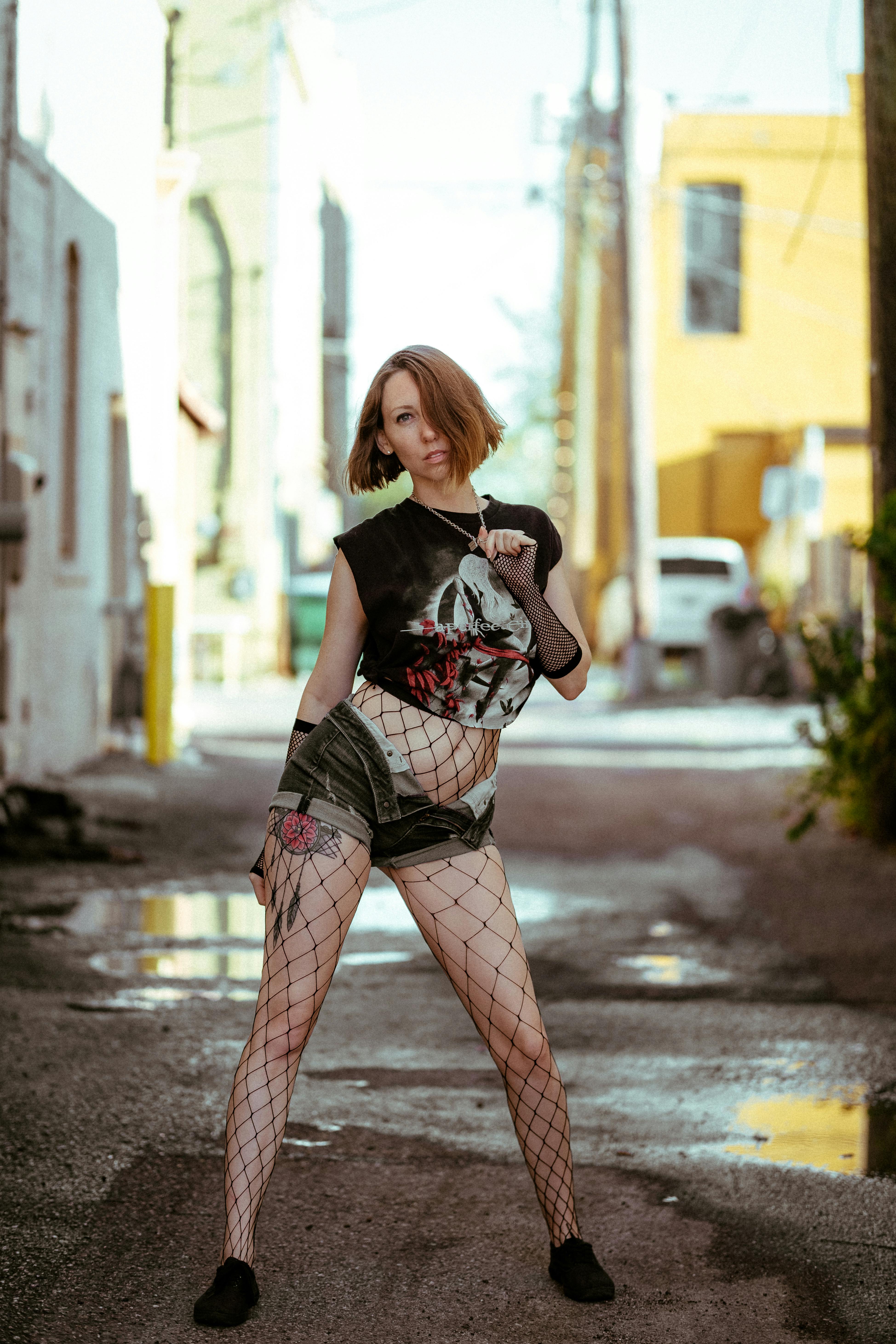 Woman in Black Crop Top Wearing Fishnet Stockings and Denim Shorts