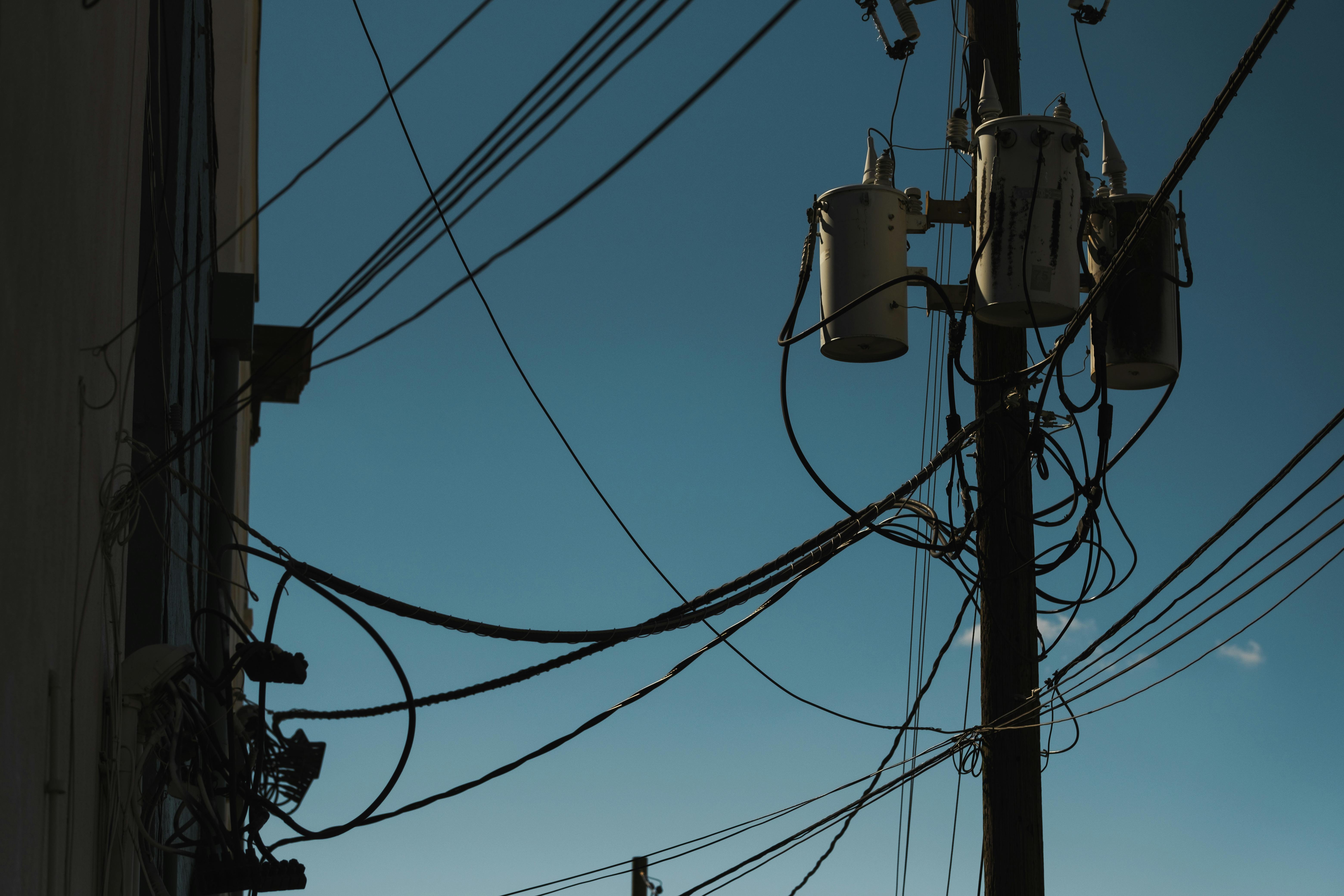 Low angle view of power lines and transformers against a clear blue sky, depicting modern electricity infrastructure.