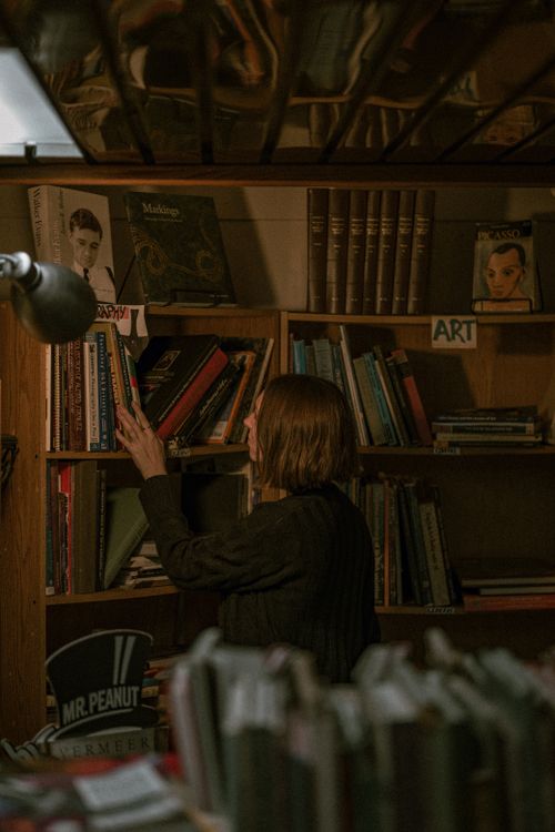 Free A woman with short hair browses bookshelves in a dimly lit home library, creating a warm and intimate atmosphere. Stock Photo