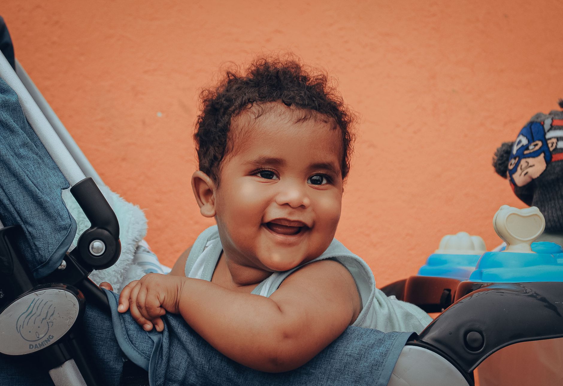 Smiling baby with curly hair sitting comfortably in a stroller, showing joy.