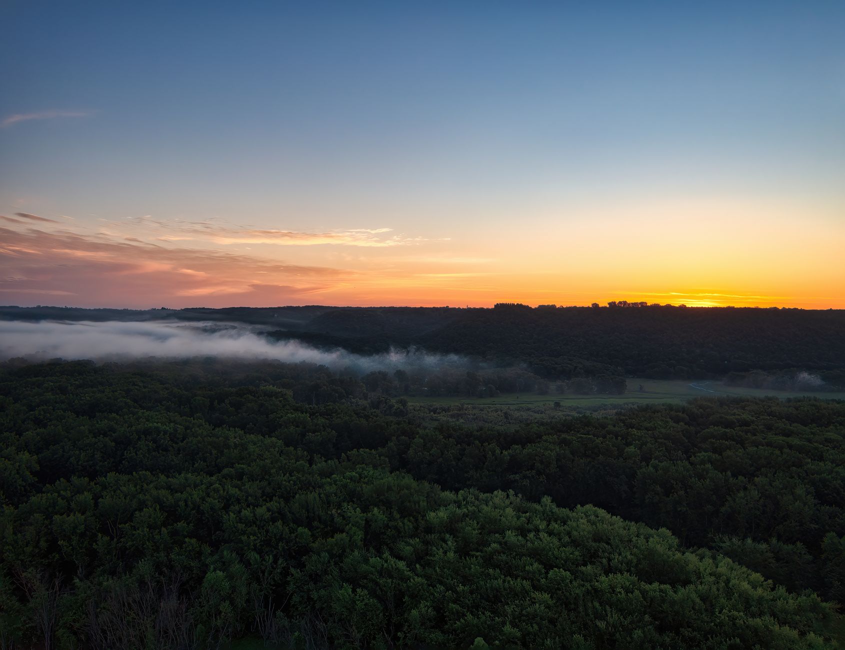 Stunning aerial view of Maiden Rock, Wisconsin at sunrise with mist over lush forest.