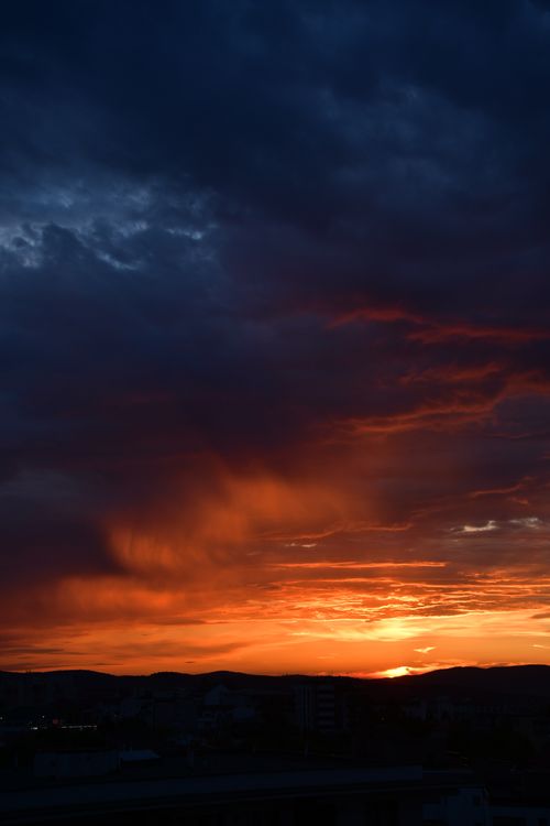 Free Vibrant sunset with dramatic dark clouds over Cluj-Napoca, creating a vivid skyscape. Stock Photo