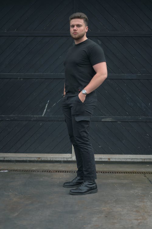 A Man in Black Shirt and Pants Standing on the Street while Looking with a Serious Face