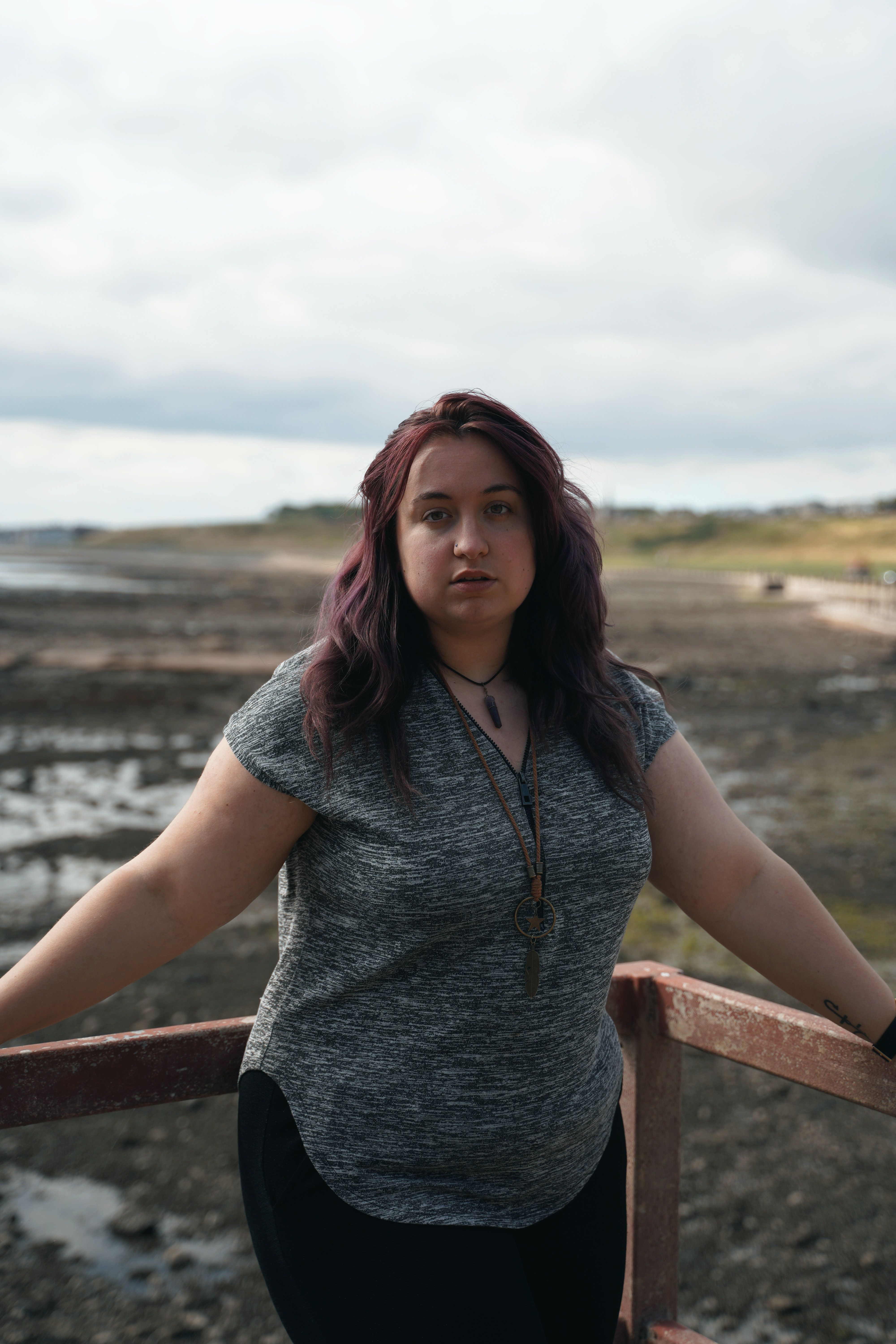 Portrait of a young woman standing by a railing with a scenic outdoor background.