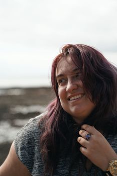 Portrait of a smiling woman with purple hair, enjoying a serene day at the beach.