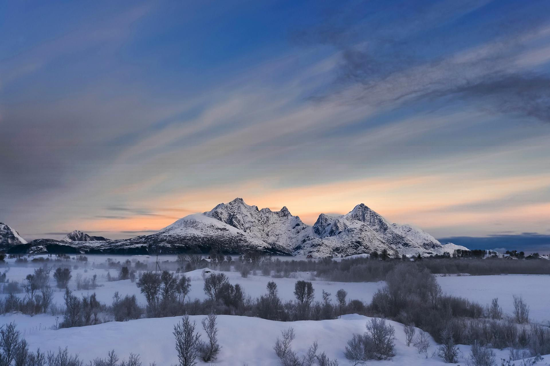 Serene snow-covered landscape of Lofoten mountains under a vibrant sunset sky in Norway.