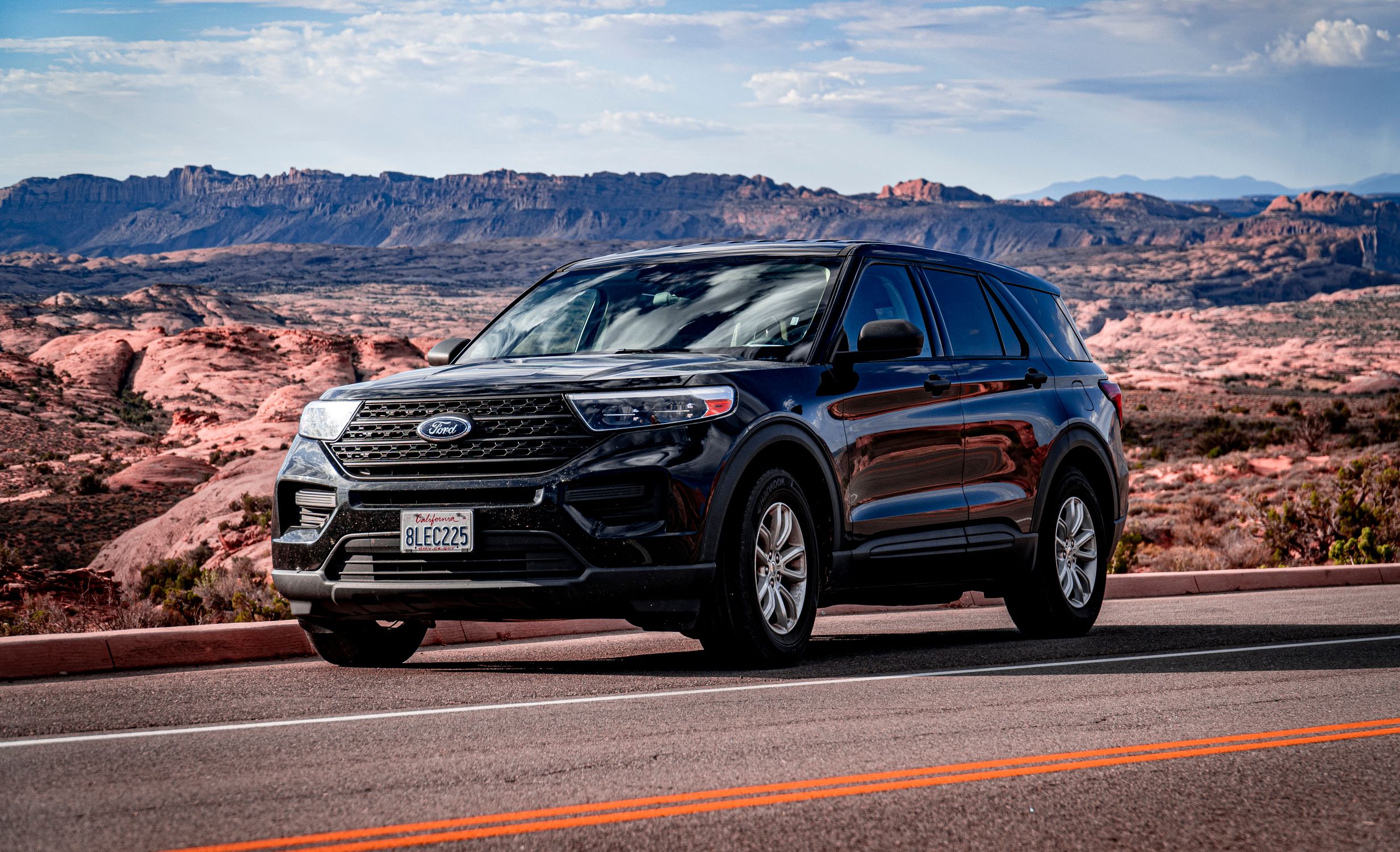 A black SUV parked on a scenic road with stunning mountain views under a cloudy sky.