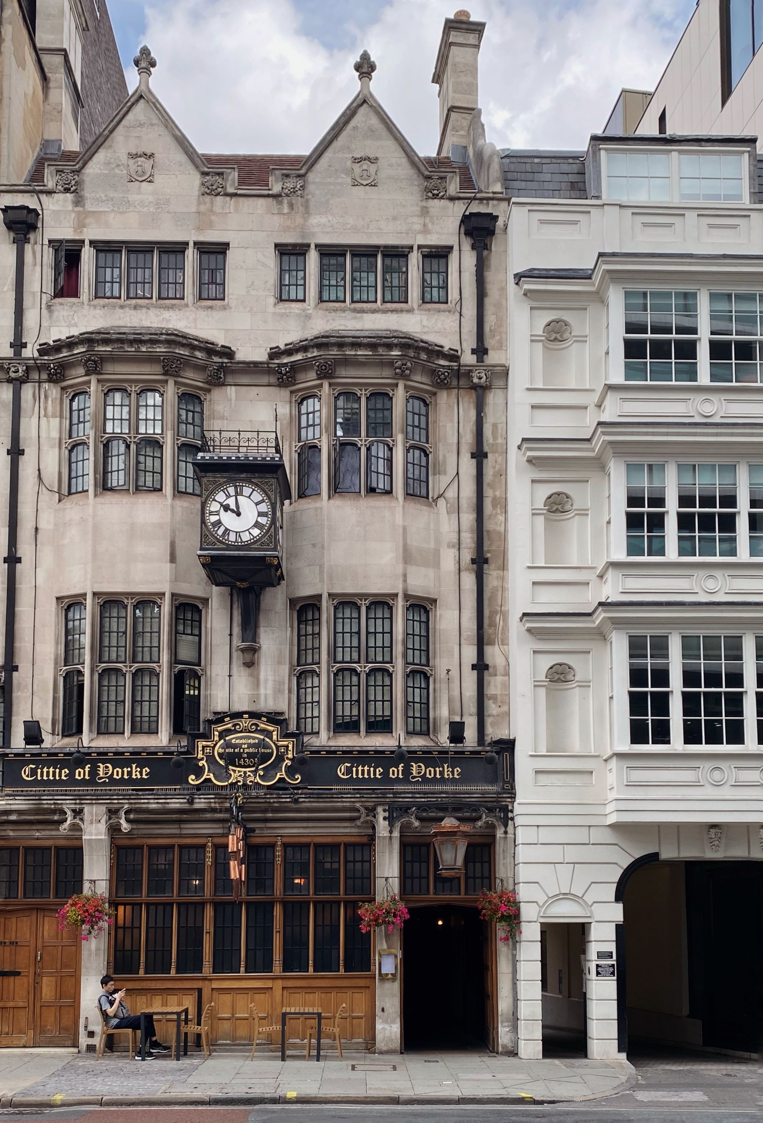 Charming old building in London with intricate facade, clock, and sidewalk cafe seating.