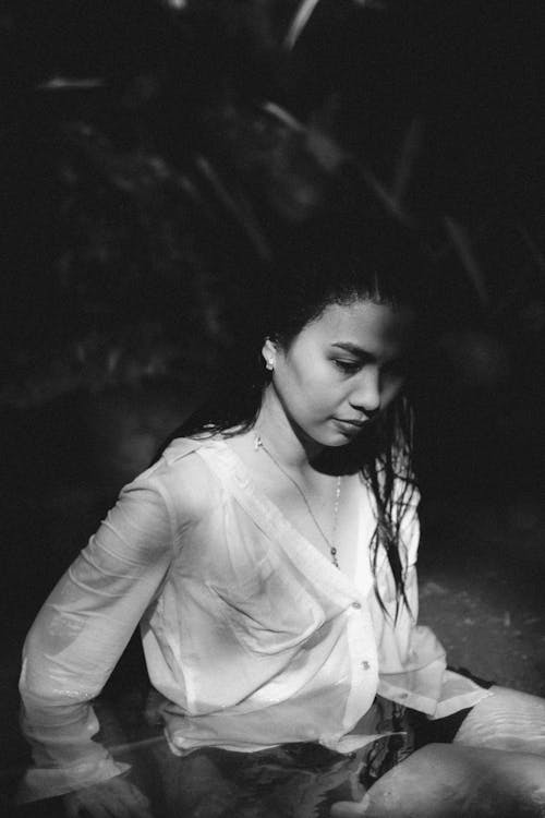 Black and White Photo of a Young Woman in a Blue Shirt Sitting in the Water