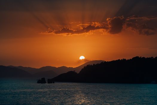 Capture of a stunning sunset with dramatic clouds and silhouetted mountains over the ocean.
