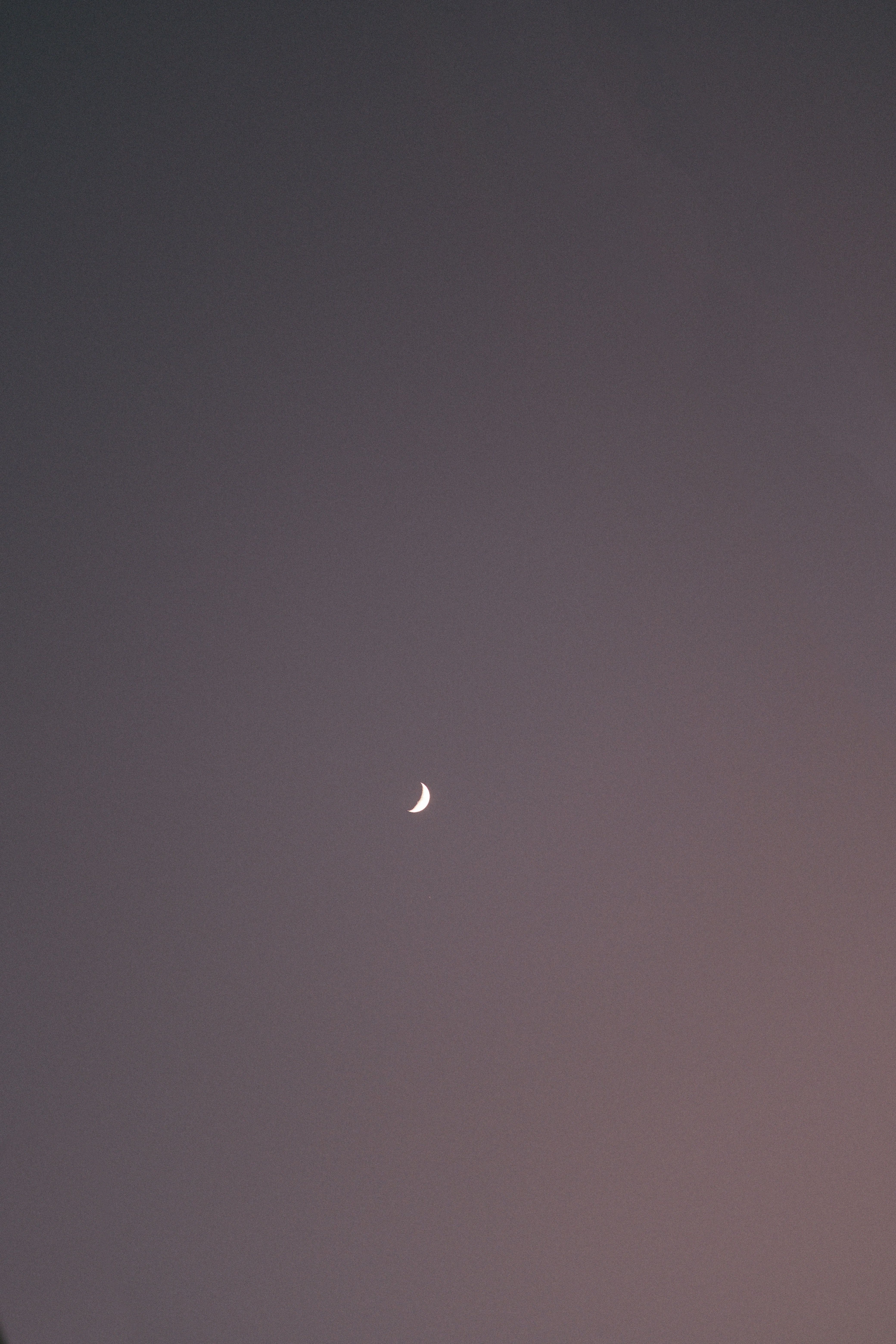 A serene crescent moon against a dark evening sky above Tulum, Mexico, creating a minimalist aesthetic.