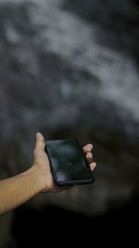 Close-up of a hand holding a smartphone outdoors, blurred background.