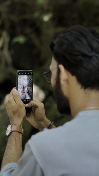A young man taking a photograph of nature using a smartphone in an outdoor setting.