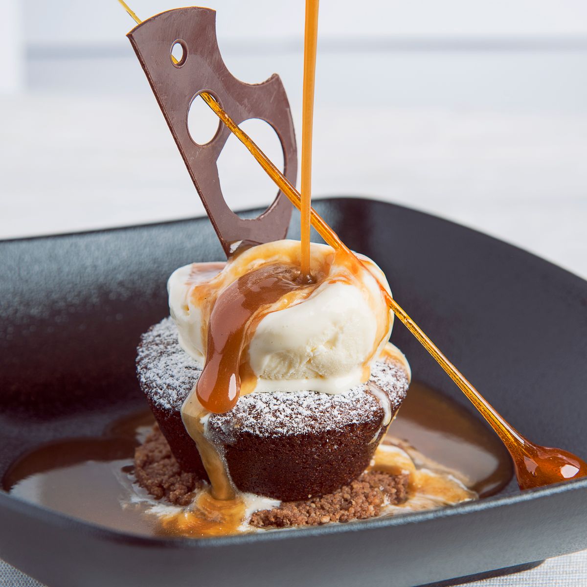 Warm sticky toffee pudding served with vanilla ice cream while golden toffee sauce is poured over the top
