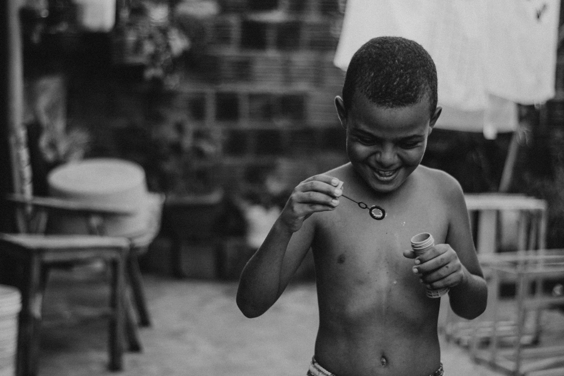 Black and white photo of a smiling child blowing bubbles, capturing a moment of joy.