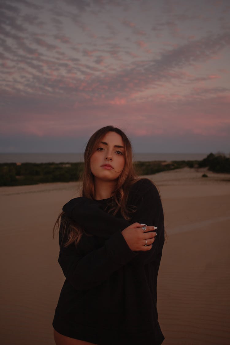 Girl With Long Hair Wearing Black Sweater Posing On A Sandy Beach At Dusk