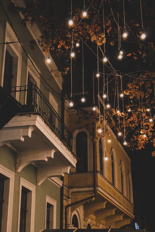 Free A picturesque European street illuminated with festive lights hanging from trees during nighttime. Stock Photo
