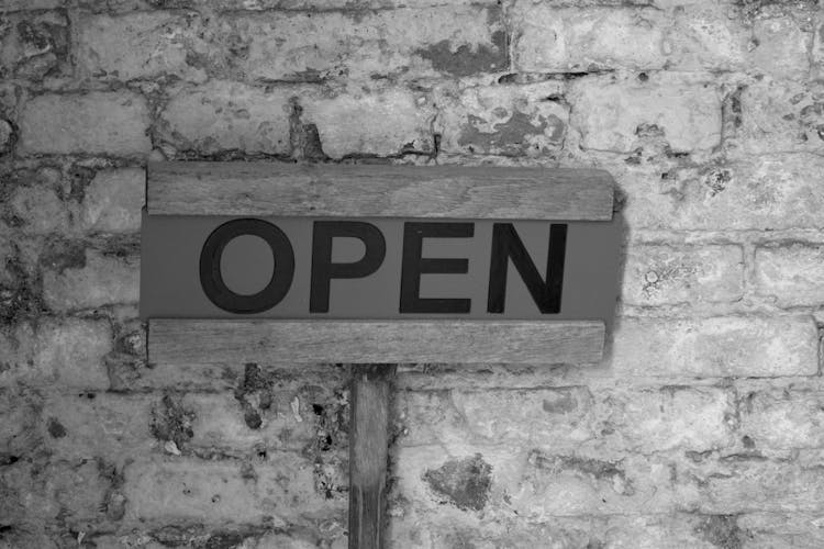 Close-up Of A Sign Saying Open On A Brick Wall 