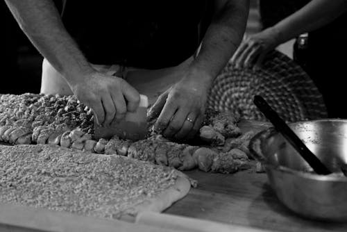 Grayscale Photo of a Person Cutting Dough