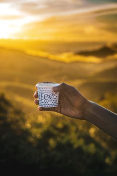 A hand holds a coffee cup against a stunning sunset in Vagamon, India, capturing a perfect golden hour moment.