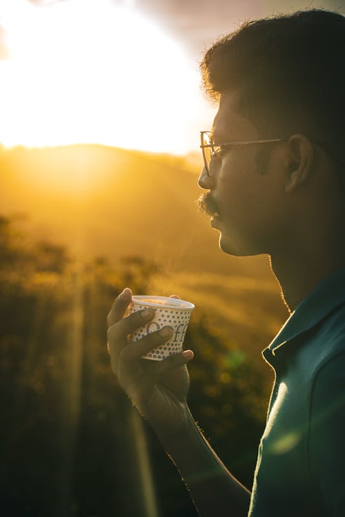 A Man Wearing Sunglasses Holding a Cup of Coffee During Golden Hour