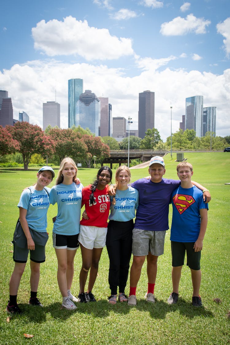 Group Of Kids Standing Together In A Park With The View Of Houston, Texas Skyline In The Background 