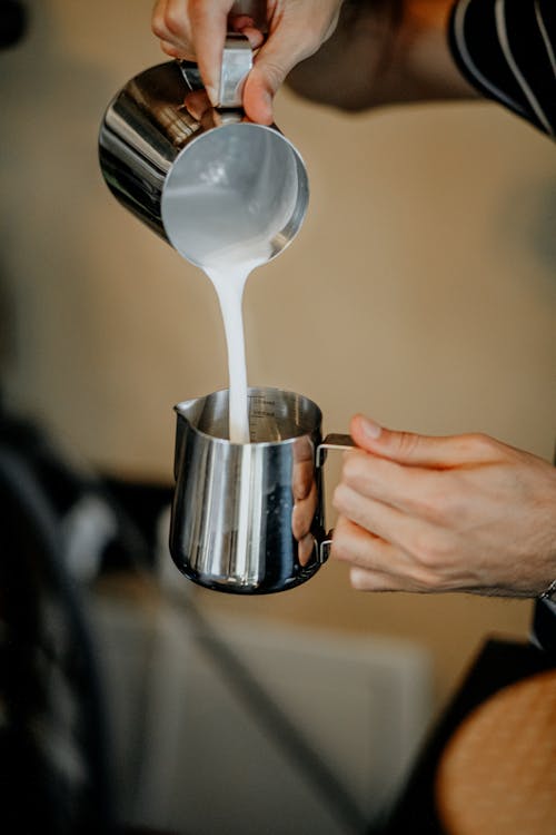Person Pouring Milk on Frothing Pitcher