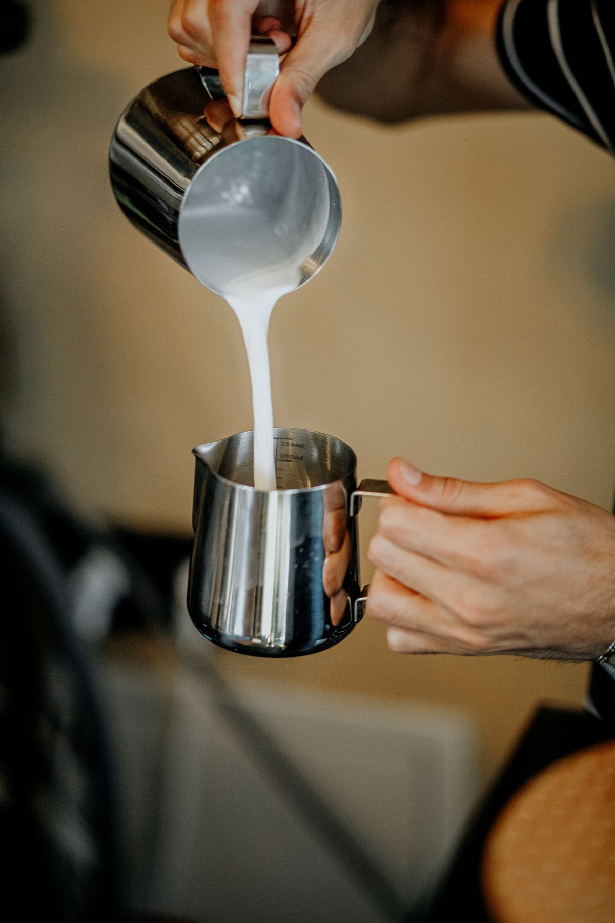 Real barista transferring textured milk between two stainless steel pitchers