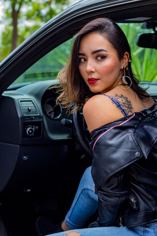 Free Confident woman with tattoo in fashionable attire sitting inside a car, looking back. Stock Photo