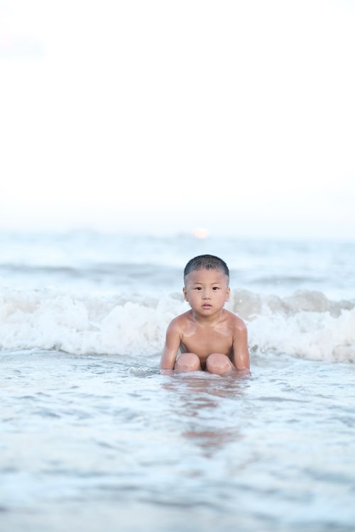 Free A young child sits quietly in the ocean waves, capturing a moment of tranquility and innocence. Stock Photo