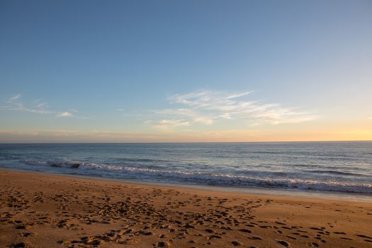 Peaceful view of Malibu beach with gentle waves and a golden sunset sky.