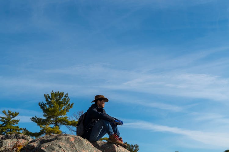 Man In Blue Jacket Sitting On Rock 